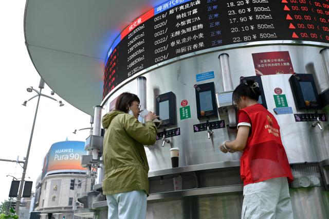 A woman (L) buys a beer from a self service beer carousal offering a variety of beer flavours along a business street in Beijing on July 2, 2026. (Photo by WANG Zhao / AFP)