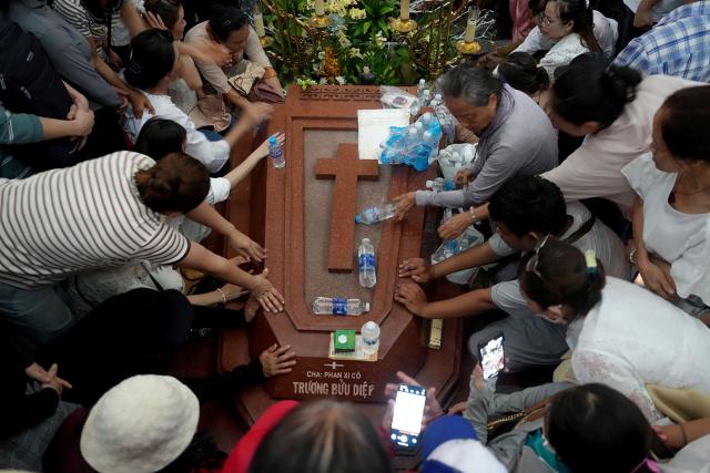 People places their hands on the grave of the late priest Francis Xavier Truong Buu Diep at the Tac Say Pilgrimage Center in Ca Mau province in southern Vietnam on July 2, 2026. Tens of thousands of Catholics flocked to a small parish in the Mekong Delta on July 2 for the first beatification ceremony held on Vietnamese soil, with an envoy of Pope Leo XIV presiding over the special mass. (Photo by AFP)