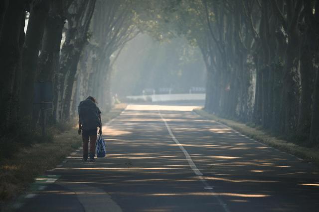 A pedestrian with a bag walks on a road closed by firefighters during a wildfire in Pouzols-Minervois, southern France on July 2, 2026. One year after the wildfire in the Corbières massif, the south of France has once again been hit by a large-scale blaze that broke out July 1, 2026 afternoon in the Herault before quickly spreading to the neighboring department of Aude under the combined effect of drought and wind, and is being fought by hundreds of firefighters. (Photo by Lionel BONAVENTURE / AFP)