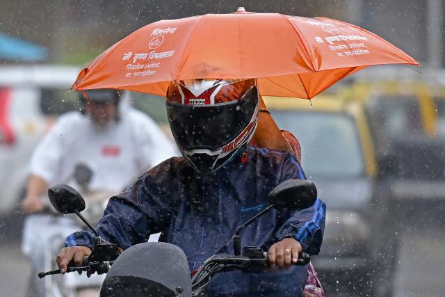 A couple rides a bike during rain showers in Mumbai on July 2, 2026. (Photo by Punit PARANJPE / AFP)
