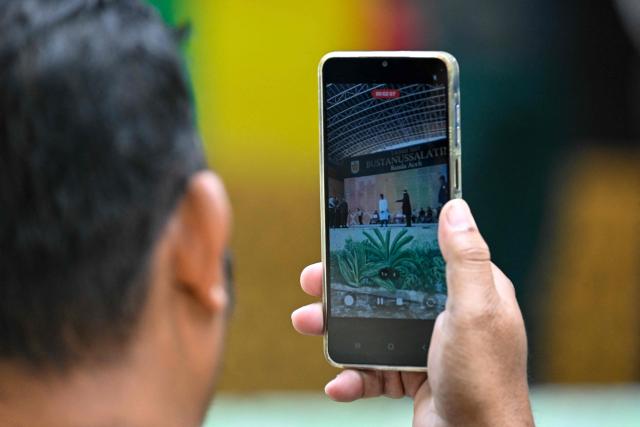 A man records a video as a man who allegedly had sexual intercourse on a TikTok livestream is caned as punishment under sharia law in Banda Aceh on July 2, 2026. (Photo by CHAIDEER MAHYUDDIN / AFP)