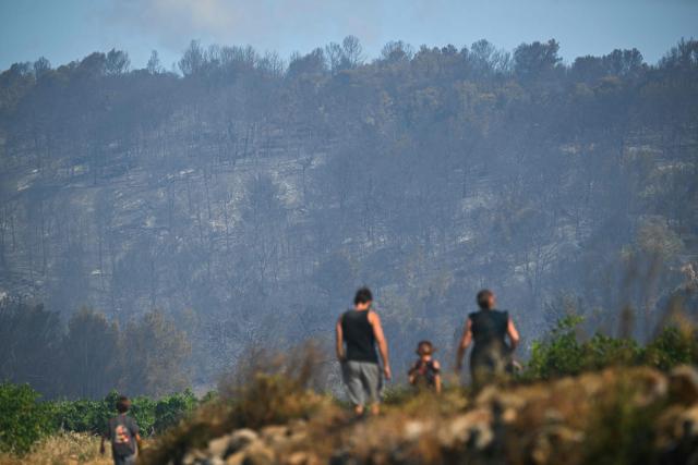 People look at mountain ranges during a wildfire in Pouzols-Minervois, southern France on July 2, 2026. One year after the wildfire in the Corbières massif, the south of France has once again been hit by a large-scale blaze that broke out on July 1, 2026 afternoon in the Herault before quickly spreading to the neighboring department of Aude under the combined effect of drought and wind, and is being fought by hundreds of firefighters. (Photo by Lionel BONAVENTURE / AFP)