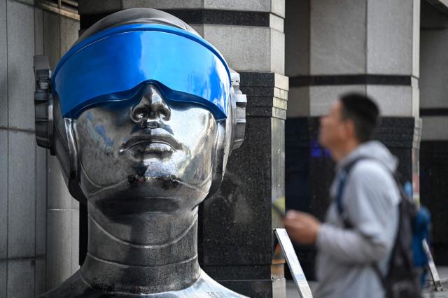 The photo taken on March 17, 2026 shows people walking past a statue at Huaqiangbei Electronic Market in Shenzhen, southern China's Guangdong province. (Photo by Jade GAO / AFP)