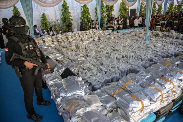 A Customs officer stands next to packages of seized cannabis buds during a press conference in Gresik, East Java Province, on July 2, 2026. The National Narcotics Agency (BNN) in collaboration with Customs and the police foiled an attempt to smuggle 3.37 metric tons of cannabis buds from Thailand and apprehended 12 suspected perpetrators. (Photo by Juni KRISWANTO / AFP)