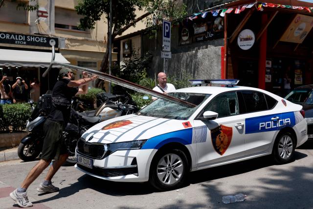Protesters destroy the windshield of a police car with a barricade as violent clashes erupted between police and demonstrators on the sidelines of a demonstration against a controversial luxury resort development linked to US President near a protected natural area, outside the parliament, in Tirana, on July 2, 2026. Since late May, protests have been held against the construction of a luxury hotel linked to Donald Trump's daughter and her husband in a nature reserve in Zvernec, on Albania's southwestern coast. For the second time this week, large groups of protesters had gathered outside the country's parliament in an attempt to confront lawmakers and block entry to the building. (Photo by Adnan Beci / AFP)