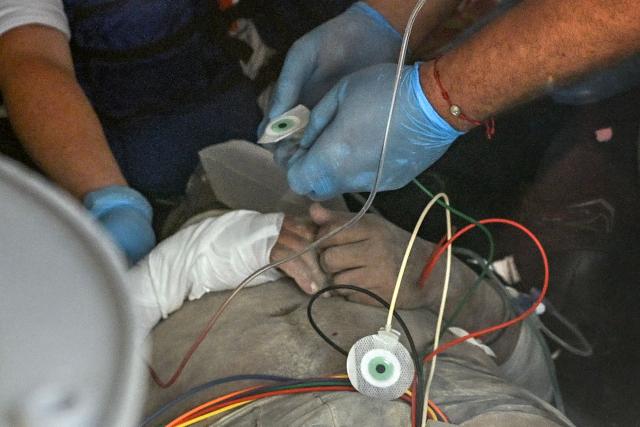 A health worker of the Red Cross assists Hernan Gil, a survivor of Venezuela's twin earthquakes, inside an ambulance in Catia La Mar, La Guaira State, Venezuela on July 2, 2026, eight days after the quake. Hernan Gil, a 43-year-old security guard, had been buried in the booth of the seven-story building where he worked in Catia La Mar, a coastal area in the state of La Guaira devastated by the disaster. (Photo by Federico PARRA / AFP)