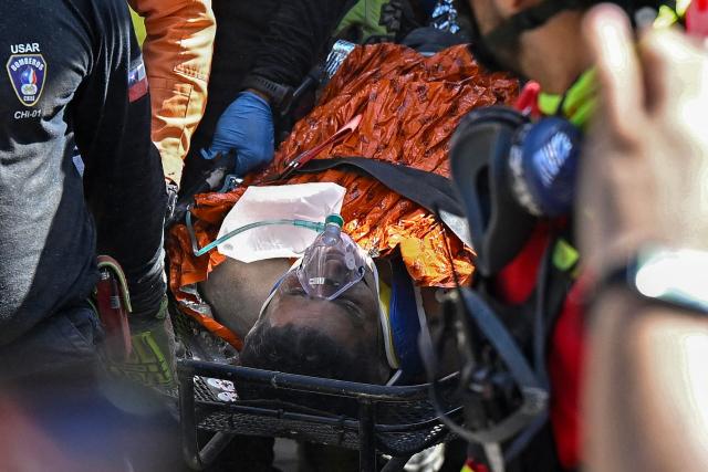 Hernan Gil, a survivor of Venezuela's twin earthquakes, is rushed into an ambulance by members of international rescue teams in Catia La Mar, La Guaira State, Venezuela on July 2, 2026, eight days after the quake. Hernan Gil, a 43-year-old security guard, had been buried in the booth of the seven-story building where he worked in Catia La Mar, a coastal area in the state of La Guaira devastated by the disaster. (Photo by Federico PARRA / AFP)