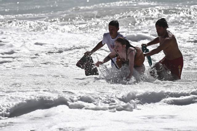 Lifeguards escort a bather (C) back to shore after rescuing her from drowning using a portable inflatable rescue device worn around her waist at the beach in Labenne, southwestern France on July 1, 2026. (Photo by Christophe ARCHAMBAULT / AFP)