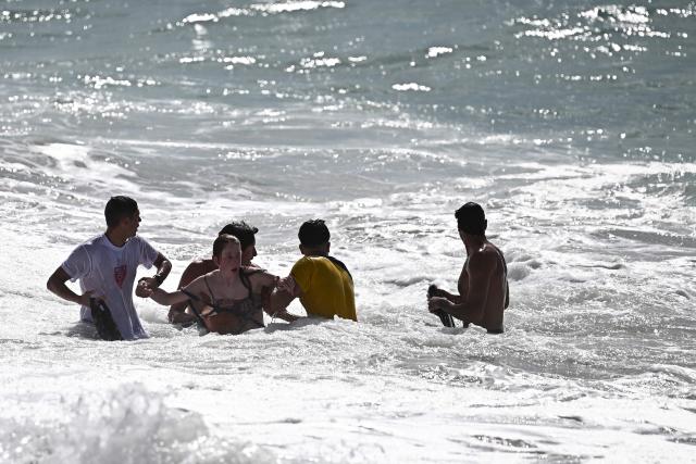 Lifeguards escort a bather (C) back to shore after rescuing her from drowning using a portable inflatable rescue device worn around her waist at the beach in Labenne, southwestern France on July 1, 2026. (Photo by Christophe ARCHAMBAULT / AFP)