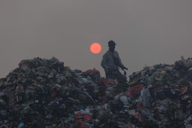 A ragpicker sorts through garbage as smoke billows from a fire at the Jatiwaringin landfill in Tangerang, Banten, on July 2, 2026. (Photo by ADITYA AJI / AFP)