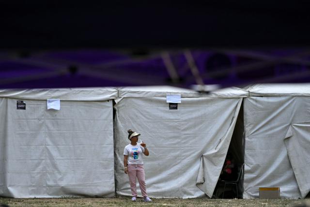 A woman stands next to tents at a displaced camp at the Ali West Park in Caracas on July 2, 2026, eight days after twin earthquakes. Hundreds of rescuers in Venezuela cheered and embraced on July 2, 2026 after pulling 43-year-old Hernan Gil from the ruins of a collapsed building eight days after deadly twin earthquakes, AFP journalists witnessed. (Photo by MARTIN BERNETTI / AFP)