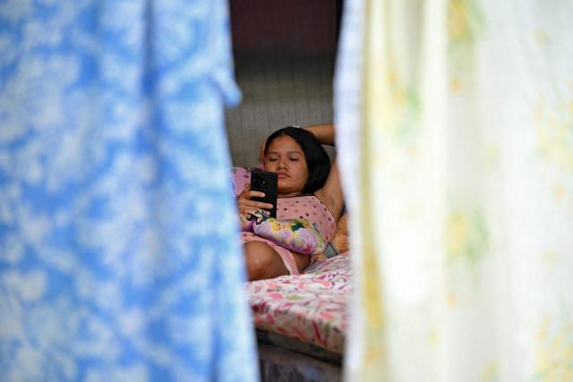 A woman looks at her mobile phone at a camp at the Ali West Park in Caracas on July 2, 2026, eight days after twin earthquakes. Hundreds of rescuers in Venezuela cheered and embraced on July 2, 2026 after pulling 43-year-old Hernan Gil from the ruins of a collapsed building eight days after deadly twin earthquakes, AFP journalists witnessed. (Photo by MARTIN BERNETTI / AFP)