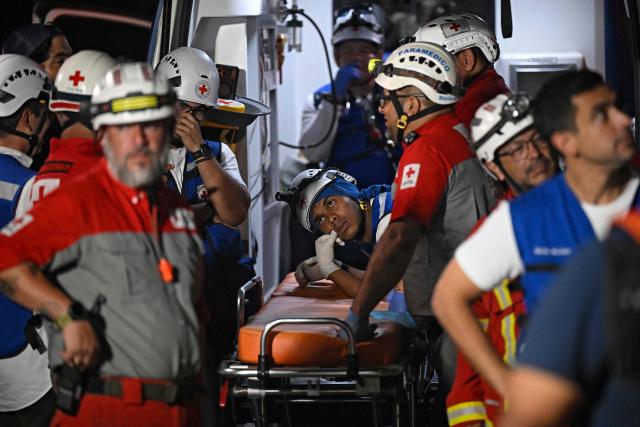 Rescue workers wait by an ambulance outside the building from where Hernan Gil was later rescued, in Catia La Mar, La Guaira State, Venezuela on July 2, 2026, eight days after twin earthquakes. Hundreds of rescuers in Venezuela cheered and embraced on July 2, 2026 after pulling 43-year-old Hernan Gil from the ruins of a collapsed building eight days after deadly twin earthquakes, AFP journalists witnessed. (Photo by Federico PARRA / AFP)