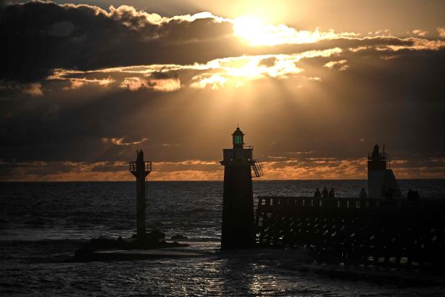 Visitors stand on the 'estacade', a wooden dike built to protect the entrance to the port, at sunset in Capbreton, southwestern France on July 1, 2026. (Photo by Christophe ARCHAMBAULT / AFP)