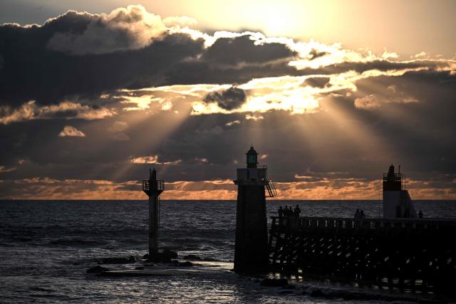 Visitors stand on the 'estacade', a wooden dike built to protect the entrance to the port, at sunset in Capbreton, southwestern France on July 1, 2026. (Photo by Christophe ARCHAMBAULT / AFP)