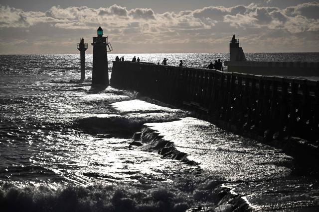 Visitors stand on the 'estacade', a wooden dike built to protect the entrance to the port, at sunset in Capbreton, southwestern France on July 1, 2026. (Photo by Christophe ARCHAMBAULT / AFP)