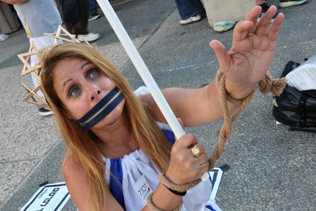 A woman stands with a symbolic zipper covering her mouth and her ropes around her hands as Israeli protesters rally against the government and the war in Gaza, at Hostage Square in Tel Aviv, on July 2, 2026, marking 1000 days since Hamas's October 7, 2023 attack on Israel. Israelis called on July 2 for a state commission of inquiry into Hamas's October 7, 2023 attack, as the country marked 1,000 days since the deadliest event in its history, which triggered the war in Gaza. A series of sombre commemorations were being held across the country, as well as protests against the government's handling of events during and after the attack. (Photo by Jack GUEZ / AFP)