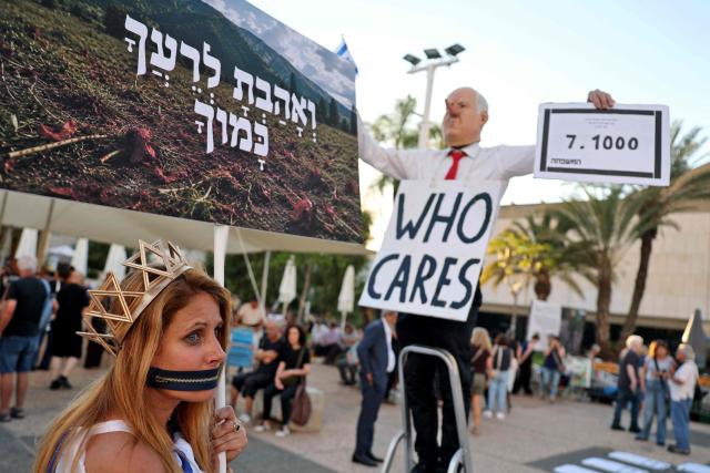 A with a symbolic zipper covering her mouth and her ropes around her hands is pictured next to a man wearing a mask depicting Israeli Prime Minister Benjamin Netanyahu during rally against the government and the war in Gaza, at Hostage Square in Tel Aviv, on July 2, 2026, marking 1000 days since Hamas's October 7, 2023 attack on Israel. Israelis called on July 2 for a state commission of inquiry into Hamas's October 7, 2023 attack, as the country marked 1,000 days since the deadliest event in its history, which triggered the war in Gaza. A series of sombre commemorations were being held across the country, as well as protests against the government's handling of events during and after the attack. (Photo by Jack GUEZ / AFP)