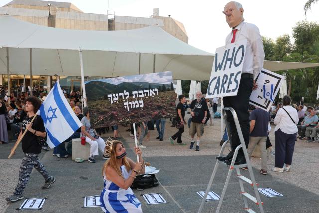 A with a symbolic zipper covering her mouth and her ropes around her hands is pictured next to a man wearing a mask depicting Israeli Prime Minister Benjamin Netanyahu during rally against the government and the war in Gaza, at Hostage Square in Tel Aviv, on July 2, 2026, marking 1000 days since Hamas's October 7, 2023 attack on Israel. Israelis called on July 2 for a state commission of inquiry into Hamas's October 7, 2023 attack, as the country marked 1,000 days since the deadliest event in its history, which triggered the war in Gaza. A series of sombre commemorations were being held across the country, as well as protests against the government's handling of events during and after the attack. (Photo by Jack GUEZ / AFP)