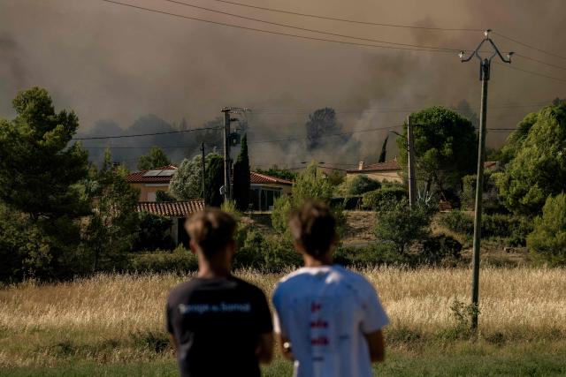 Youth watch smoke rising from a wildfire raging near houses in Pouzols-Minervois, southwestern of France, on July 2, 2026. Hundreds of firefighters are battling wildfires in the south that are being fueled by wind, drought, and heat. The largest fire is in the Aude department, but there are also fires north of Marseille, where Prime Minister is expected to chair a new interministerial crisis task force. (Photo by Idriss Bigou-Gilles / AFP)