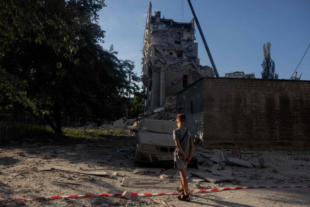 A boy stands next to a fallen red and white warning tape with a damaged car and a damaged building in the background following a Russian air attack on the Ukrainian capital of Kyiv on July 2, 2026, amid the Russian invasion in Ukraine. (Photo by Tetiana DZHAFAROVA / AFP)