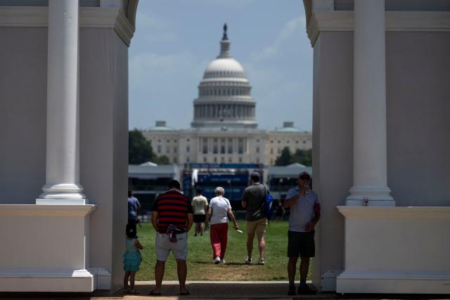 People seek shade under a replica of President Trump’s planned “Triumphal Arch” as they visit the "Great American State Fair" on the National Mall in Washington, DC, on July 2, 2026, ahead of the upcoming July 4 holiday. Americans sweltered under furnace-like temperatures this week as central and eastern cities hunkered down for a heat wave set to last through the July 4 holiday weekend. Dozens of local temperature records could be broken, the National Weather Service (NWS) warned, with temperatures in many places to surpass 100 degrees Fahrenheit (38 degrees Celsius) and high humidity pushing the heat index as high as 115 degrees. (Photo by Kent Nishimura / AFP)