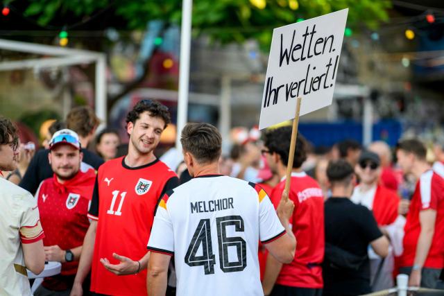 A Germany fan holds up a placard with the lettering 'I bet you are going to lose' as he speaks with an Austria supporter during a public screening of Austria's match against Spain played at the 2026 FIFA World Cup Los Angeles Stadium, Inglewood, USA, along the Danube Canal in Vienna on July 2, 2026. (Photo by MAX SLOVENCIK / APA / AFP) / Austria OUT