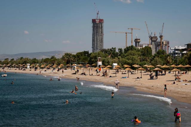 People visit a beach of the southern Athenian suburb of Glyfada on June 26, 2026, as a 200-meter-tall, 50-story skyscraper towers which is is the tallest building ever constructed in Athens is seen in the background. Less than 15 km from the center of Athens, Glyfada—like many neighborhoods along the Saronic Gulf—has seen its population grow in recent years due to a major real estate development underway in the neighboring municipality of Ellinikon, leading to skyrocketing prices.
Nicknamed “The Athenian Riviera”, this massive development project, spanning an area of 6.2 kmІ, will soon include hotels, shopping centers, parks, marinas, 8,000 housing units, and a “new city” of 30,000 residents, according to Lamda Development, the company in charge. (Photo by Aris MESSINIS / AFP)