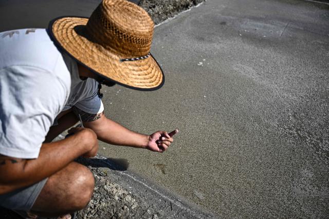 French salt maker Simon Poinot checks the salinity of a basin before harvesting salt flower which forms a thin crust on the surface of seawater drained through the basins of a salt marsh in Chateau-d'Olйron, on the Oleron Island, south-western France on June 17, 2026. The profession of salt worker, which disappeared from Olйron Island in the 1980s, was reintroduced with the support of local authorities because salt marshes, as “buffer” zones, can absorb part of the marine flooding, which is becoming increasingly frequent with climate change. (Photo by Christophe ARCHAMBAULT / AFP)