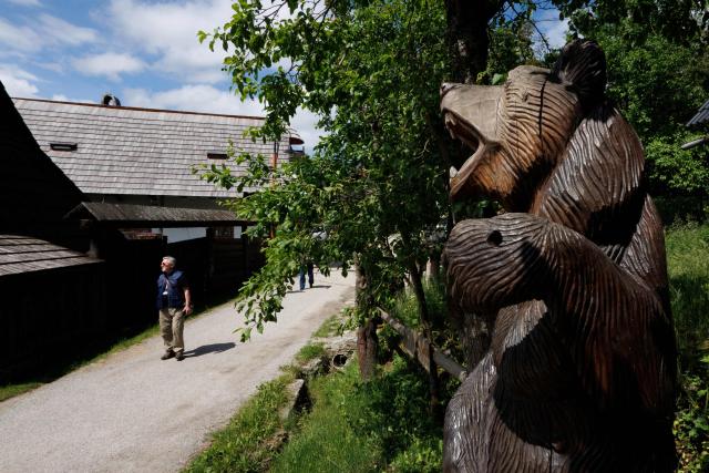 A tourist walks past log houses and a bear sculpture at the UNESCO-listed Slovak village of Vlkolinec, near the Central Slovakian town of Ruzomberok on June 6,2026. The village Vlkolinec was recognized by UNESCO in 1993 and with 45 original houses is one of the three preserved groups of wooden houses in Central Europe on the World Heritage list, along with two other sites located in Hungary and the Czech Republic. (Photo by Joe KLAMAR / AFP)