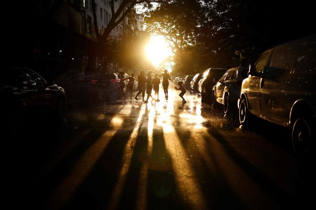 People jump on water-soaked pavement around an open fire hydrant at sunset in the Hamilton Heights neighborhood of the Manhattan borough of New York City on July 2, 2026, during a heatwave. Blistering temperatures and humidity gripped swaths of the United States on July 1, with the worst yet to come for the densely populated East Coast as the nation co-hosts the World Cup and prepares to celebrate its 250th birthday. "Heat dome" conditions -- in which high-pressure systems trap warm air like the lid on a pot -- persisted over the Midwest and South and were moving east, with some 46 million people under heat alerts. (Photo by CHARLY TRIBALLEAU / AFP)