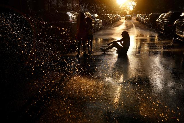 A person sits in pooled water as spray from an open fire hydrant fills the air in the Hamilton Heights neighborhood of the Manhattan borough of New York City on July 2, 2026, during a heatwave. Blistering temperatures and humidity gripped swaths of the United States on July 1, with the worst yet to come for the densely populated East Coast as the nation co-hosts the World Cup and prepares to celebrate its 250th birthday. "Heat dome" conditions -- in which high-pressure systems trap warm air like the lid on a pot -- persisted over the Midwest and South and were moving east, with some 46 million people under heat alerts. (Photo by CHARLY TRIBALLEAU / AFP)
