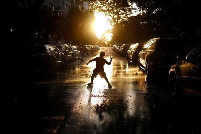 A kid plays on water-soaked pavement around an open fire hydrant at sunset in the Hamilton Heights neighborhood of the Manhattan borough of New York City on July 2, 2026, during a heatwave. Blistering temperatures and humidity gripped swaths of the United States on July 1, with the worst yet to come for the densely populated East Coast as the nation co-hosts the World Cup and prepares to celebrate its 250th birthday. "Heat dome" conditions -- in which high-pressure systems trap warm air like the lid on a pot -- persisted over the Midwest and South and were moving east, with some 46 million people under heat alerts. (Photo by CHARLY TRIBALLEAU / AFP)