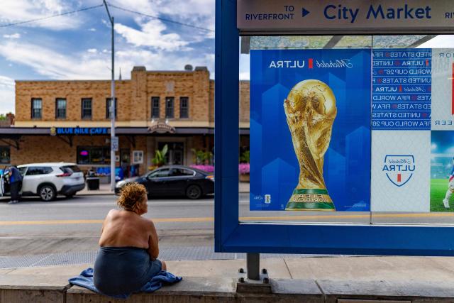 A woman rests next to sign with a poster of the World Cup tournament in Kansas City on July 2, 2026. (Photo by Odd Andersen / AFP)