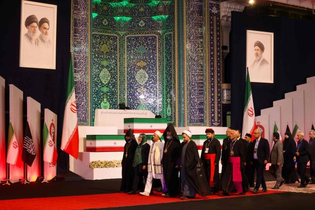 Local and foreign officials walk past the coffins of Iran's slain supreme leader Ali Khamenei and his family members after paying their respects at the Grand Mosalla in Tehran on July 3, 2026. The body of Iran's supreme leader Ali Khamenei, who was killed in US-Israeli strikes, arrived at Tehran's Grand Mosalla religious complex ahead of his funeral, state media reported on July 3. (Photo by Atta KENARE / AFP) / 
