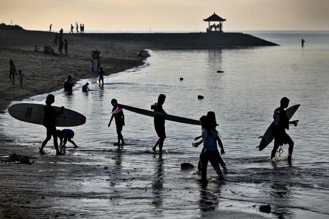 Tourists walk with their surfboards on a beach in Sanur on Indonesia's resort island of Bali on July 3, 2026. (Photo by SONNY TUMBELAKA / AFP)