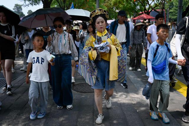 A woman (C), wearing Qing dynasty costume, walks along a road near the Forbidden City on a hot day in Beijing on July 3, 2026. (Photo by WANG Zhao / AFP)