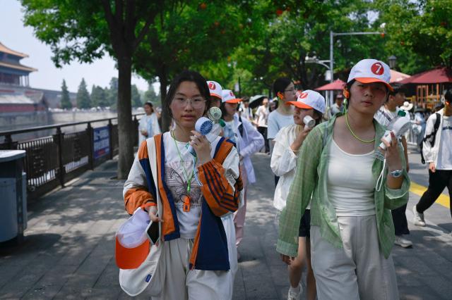 A group of tourists walk along a road after visiting the Forbidden City on a hot day in Beijing on July 3, 2026. (Photo by WANG Zhao / AFP)