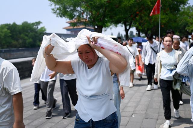 A woman uses her shirt to shelter from the sun as she walk down a road after visiting the Forbidden City on a hot day in Beijing on July 3, 2026. (Photo by WANG Zhao / AFP)