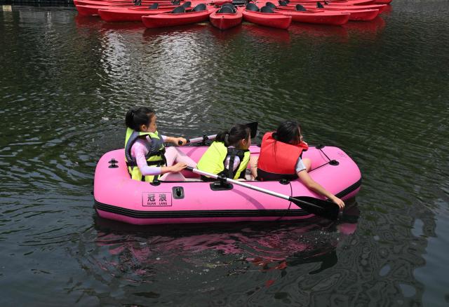 Girls row an inflatable boat on the Liangma River during summer in Beijing on July 3, 2026. (Photo by ADEK BERRY / AFP)
