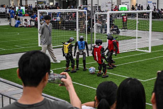 Spectators watch robots taking part in a football match at RoboCup 2026, a robotics and Artificial Intelligence (AI) competition in Incheon on July 3, 2026. (Photo by Jade GAO / AFP)