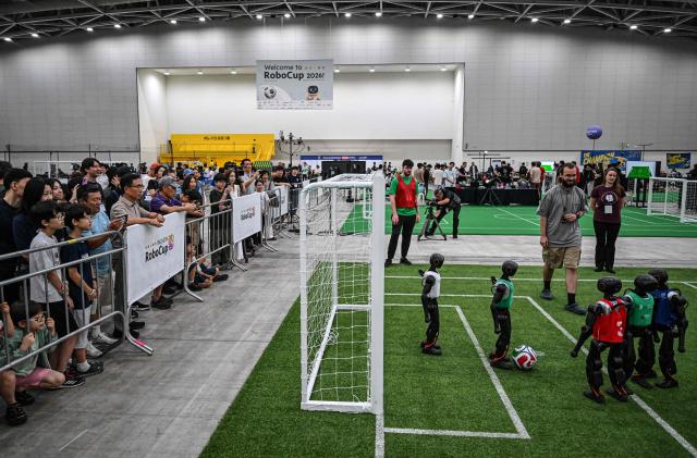 Spectators watch robots taking part in a football match at RoboCup 2026, a robotics and Artificial Intelligence (AI) competition in Incheon on July 3, 2026. (Photo by Jade GAO / AFP)
