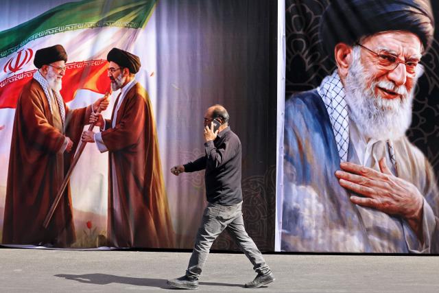 A man walks past a billboard featuring the images of Iran's slain supreme leader Ali Khamenei and his son, the current supreme leader Mojtaba Khamenei, along the street in Tehran on July 3, 2026. Preparations for the funeral of Iran's slain supreme leader Ali Khamenei were in full swing on July 3, with authorities expecting millions and a coterie of foreign dignitaries to attend the official ceremony. (Photo by ATTA KENARE / AFP) / 