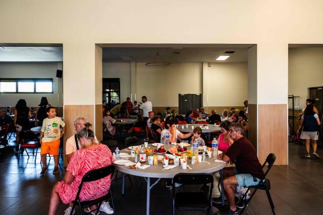 Tourists and evacuated residents have a breakfast at a reception center in Canet-en-Roussillon, the day after a wildfire broke out in the south of France, on July 3, 2026. Nearly 3,000 people had to be evacuated from several campsites, as well as from businesses and several municipalities, after a fire broke out in Sainte-Marie-la-Mer and spread on to Canet-en-Roussillon, affecting the watersports hub, firefighters and the prefect of Pyrenees-Orientales said on July 2, 2026. (Photo by Jc Milhet / AFP)