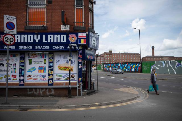 A man walks past a shop adjacent to hoardings surrounding the former Central Retail Park, which ceased trading in 2019 and has had planning approved to construct the Manchester Digital Campus, in Manchester, north west England on July 3, 2026. Andy Burnham, the recently elected MP for Makerfield who is widely expected to succeed Keir Starmer as Prime Minster, has pledged to set up a new No.10 North which will aim to devolve aspects of the Government's operation, currently based in Westminster, to the north of England. The Proposed Manchester Digital Campus will bring together around 8,800 staff from multiple government departments with a focus on digital work and has been suggested as a potential site. (Photo by Oli SCARFF / AFP)