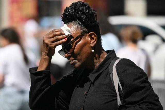 A woman wipes sweat from her face as she walks through Midtown Manhattan during a heatwave in New York City on July 3, 2026. Blistering temperatures and humidity has gripped swaths of the United States this week, with more to come for the densely populated East Coast as the nation co-hosts the World Cup and prepares to celebrate its 250th birthday on July 4. The heat wave that has been broiling the Midwest is intensifying in the Northeast, with temperatures surpassing 100F (38C) in cities including New York, Philadelphia and Washington. (Photo by ANGELA WEISS / AFP)