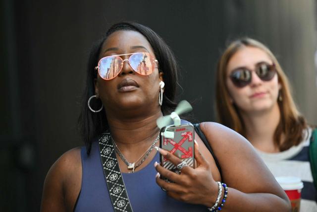 A woman uses a small portable fan attached to her phone as she walks through Midtown Manhattan during a heatwave in New York City on July 3, 2026. Blistering temperatures and humidity has gripped swaths of the United States this week, with more to come for the densely populated East Coast as the nation co-hosts the World Cup and prepares to celebrate its 250th birthday on July 4. The heat wave that has been broiling the Midwest is intensifying in the Northeast, with temperatures surpassing 100F (38C) in cities including New York, Philadelphia and Washington. (Photo by ANGELA WEISS / AFP)