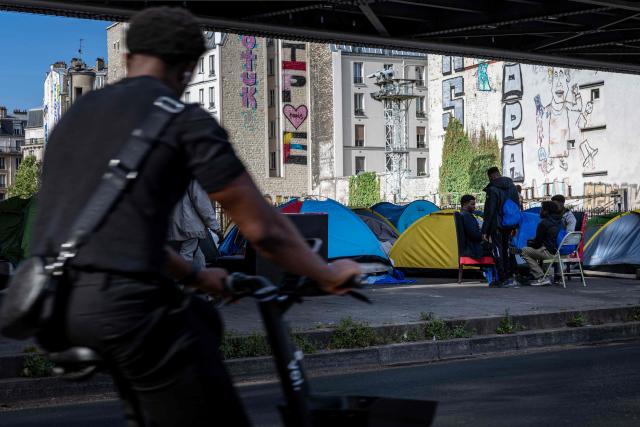 A man cycles past a makeshift camp set up beneath the elevated Stalingrad metro station in Paris on July 3, 2026. (Photo by JOEL SAGET / AFP)