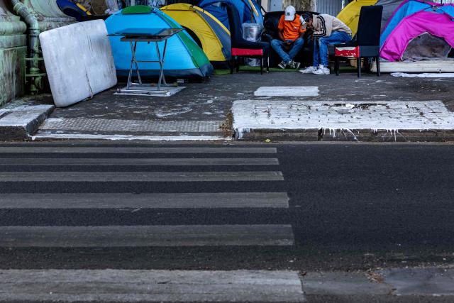 Homeless men look at their mobile phones at a makeshift camp set up beneath the elevated Stalingrad metro station in Paris on July 3, 2026. (Photo by JOEL SAGET / AFP)