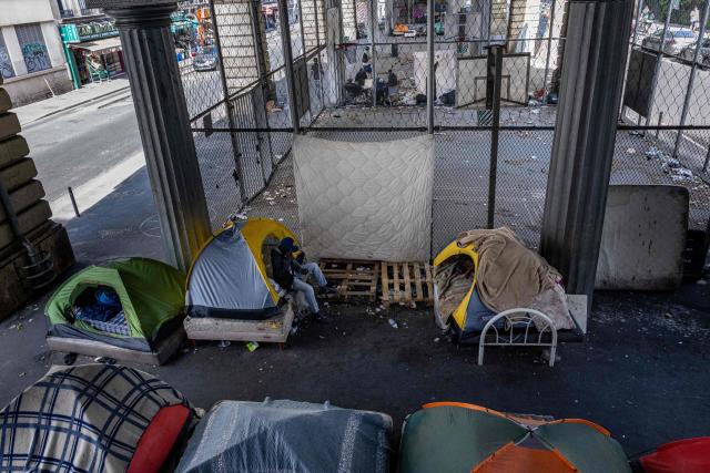 A homeless man sits at the entrance of a tent at a makeshift camp set up beneath the elevated Stalingrad metro station in Paris on July 3, 2026. (Photo by JOEL SAGET / AFP)